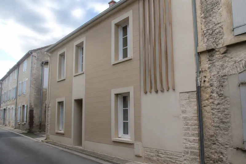 Maison de village avec bardage composite beige posé sur une façade en pierre voisine