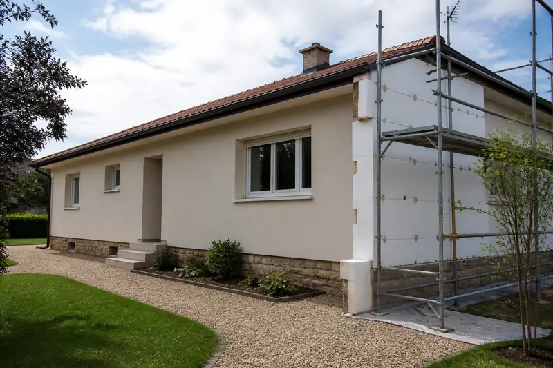 Façade de pavillon en cours d'isolation par l'extérieur sous enduit, avec plaques blanches collées et chevillées